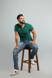Photo of Handsome young man sitting on stool against light grey background