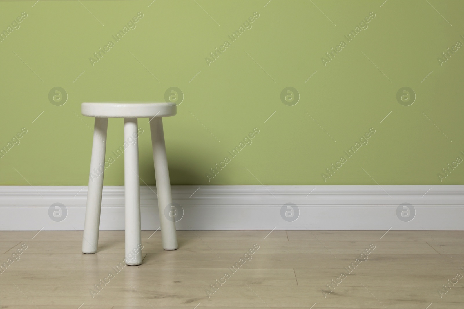 Photo of Stylish white stool near light green wall indoors. Space for text