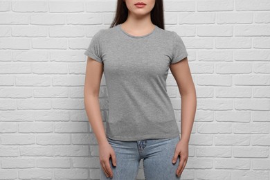 Photo of Woman wearing stylish gray T-shirt near white brick wall, closeup