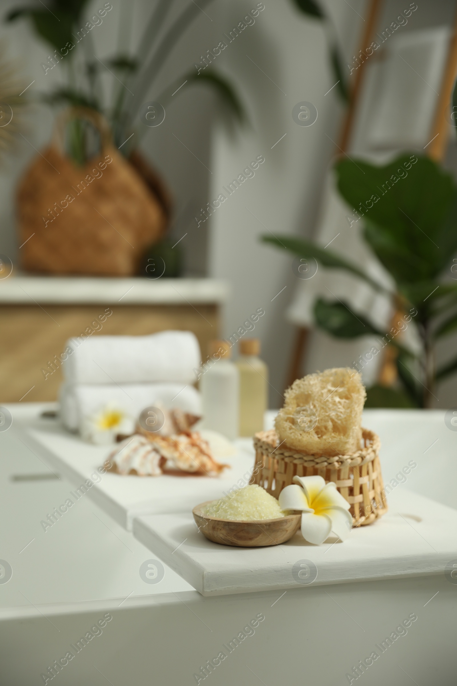 Photo of Bath tray with spa products and plumeria flower on tub in bathroom, space for text