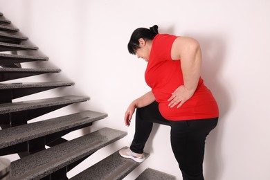 Photo of Overweight mature woman suffering from pain in left side while running upstairs indoors