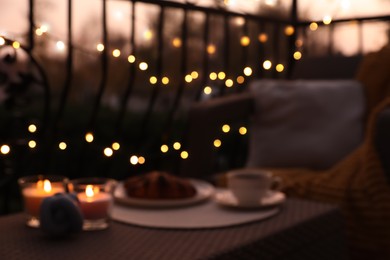 Photo of Blurred view of garden furniture with pillow, soft blanket and burning candles at balcony