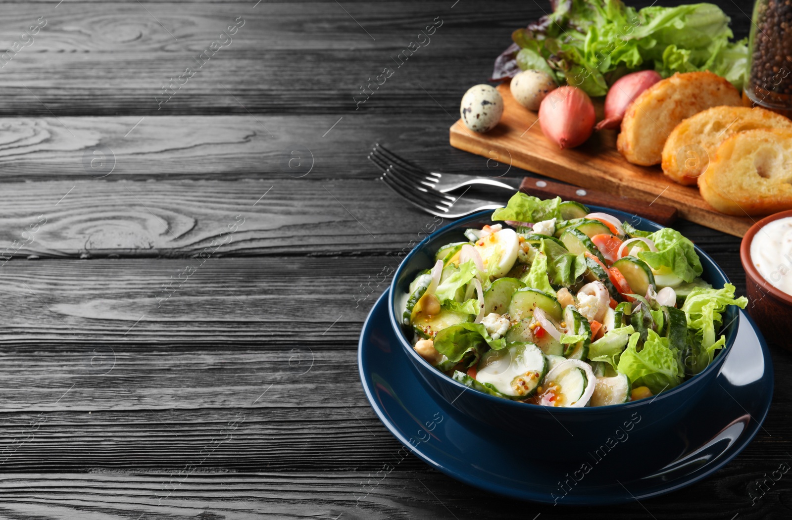 Photo of Bowl of delicious cucumber salad served on black wooden table. Space for text