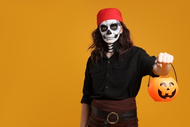 Photo of Man in scary pirate costume with skull makeup and pumpkin bucket on orange background, space for text. Halloween celebration