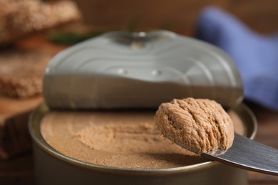 Open tin can with meat pate and knife on table, closeup