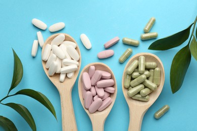 Photo of Different vitamin pills in spoons and green leaves on light blue background, flat lay