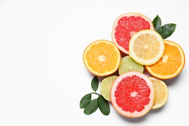 Photo of Different cut citrus fruits and leaves on white table, flat lay. Space for text