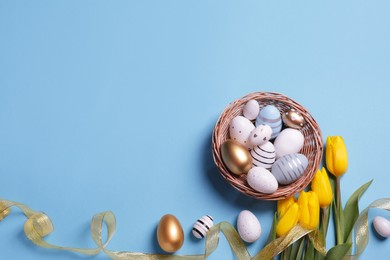 Many painted Easter eggs, tulip flowers and ribbon on light blue background, flat lay. Space for text