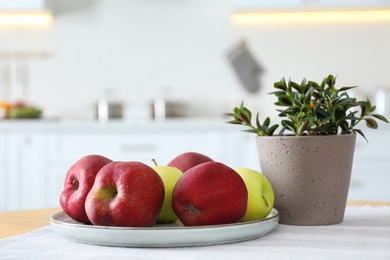 Fresh ripe apples and plant on table in kitchen