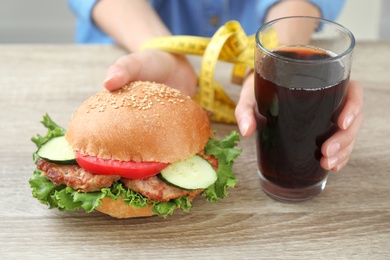 Photo of Woman with tied hands holding tasty sandwich and glass of cold drink at wooden table. Healthy diet