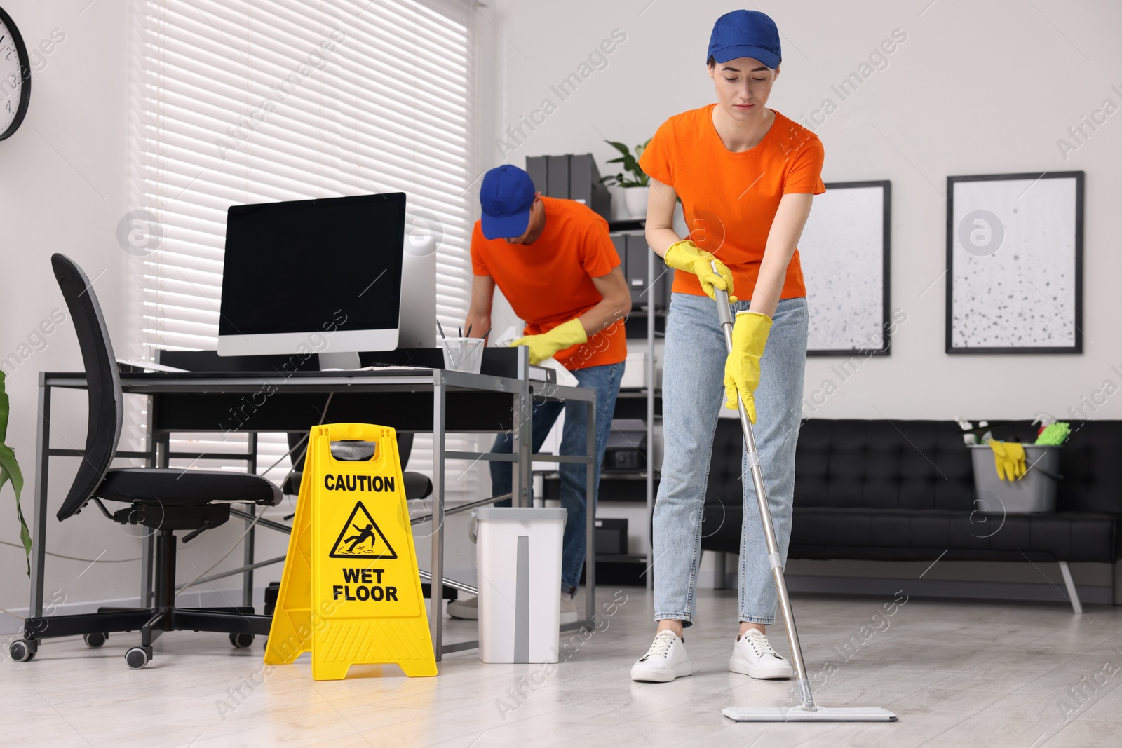 Photo of Cleaning service workers cleaning. Bucket with supplies and wet floor sign in office