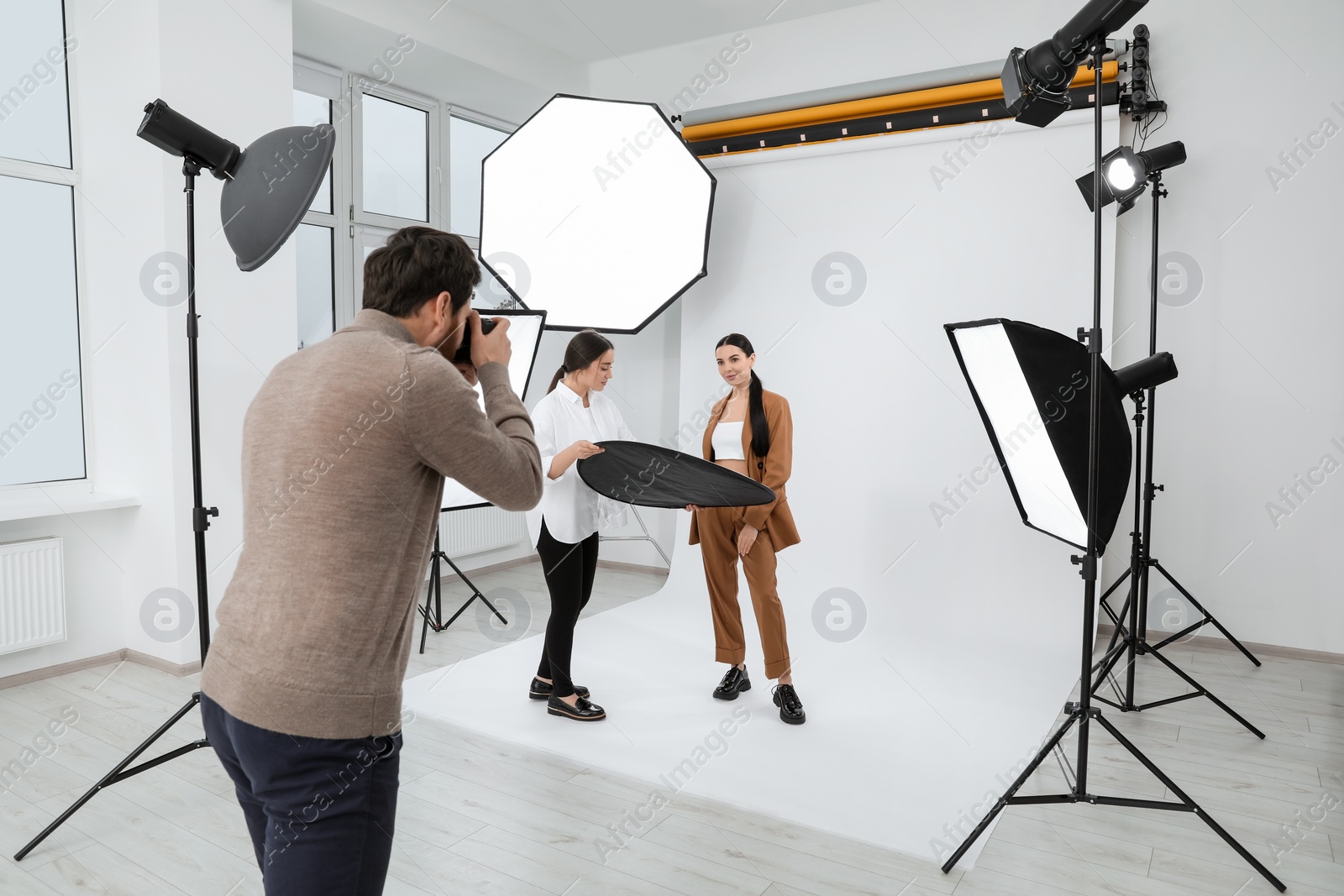 Photo of Professional photographer and assistant working with beautiful model in modern photo studio