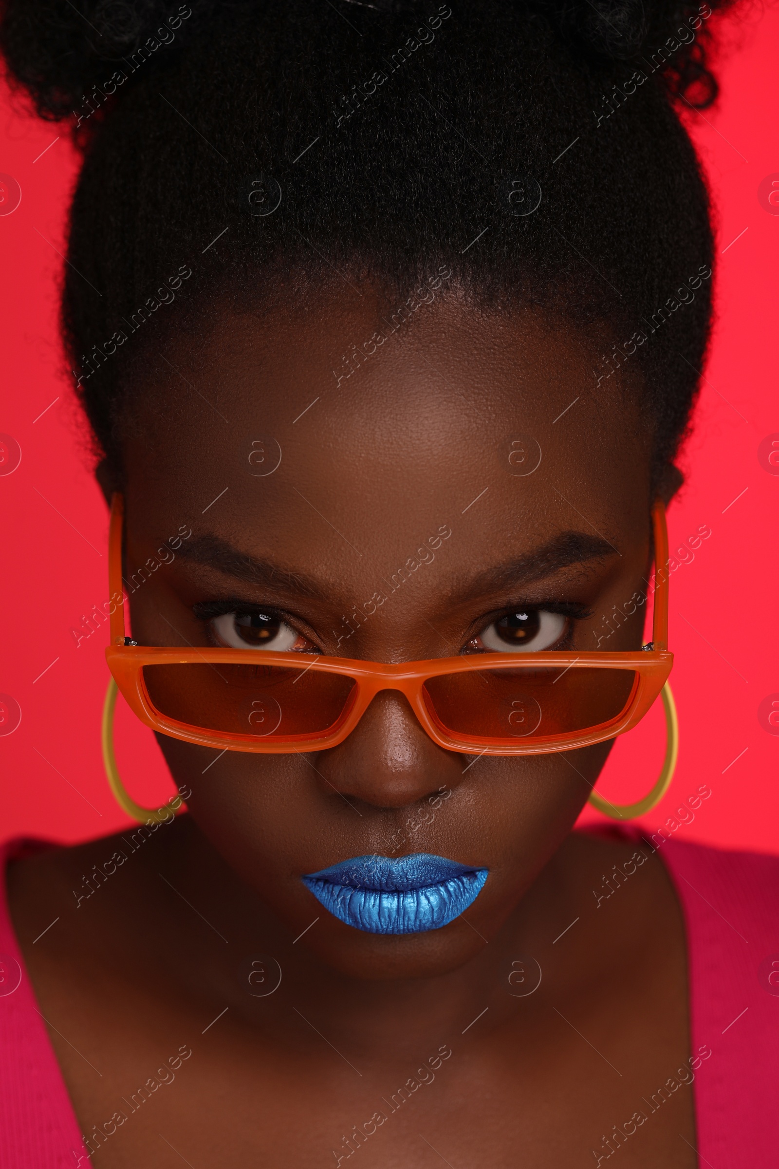 Photo of Fashionable portrait of beautiful woman with stylish sunglasses on coral background, closeup