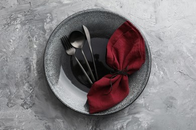 Stylish setting with cutlery, napkin and plate on grey textured table, top view