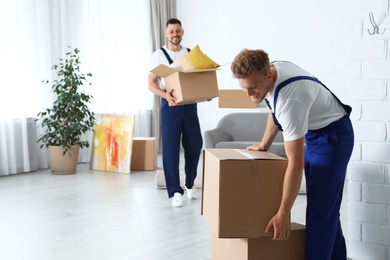 Photo of Moving service employees with cardboard boxes in room