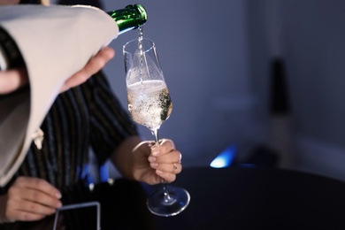 Waiter pouring champagne from bottle into woman's glass at bar, closeup. Space for text