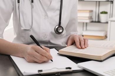 Photo of Medical student in uniform studying at table indoors, closeup