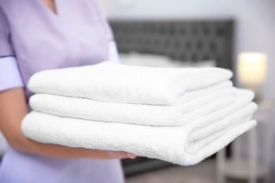 Photo of Young maid holding stack of towels in hotel room, closeup