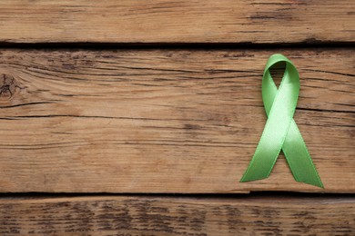 World Mental Health Day. Green ribbon on wooden background, top view with space for text