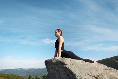 Beautiful young woman practicing yoga on rock in mountains