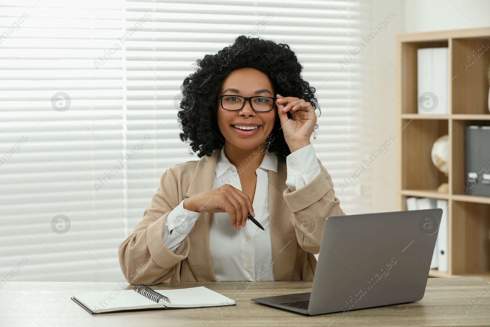 Photo of Happy young woman with laptop at wooden desk indoors