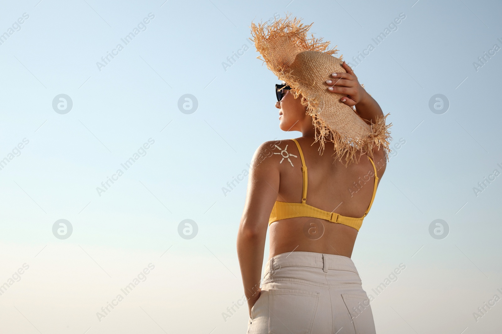 Photo of Young woman with sun protection cream on shoulder against blue sky, back view