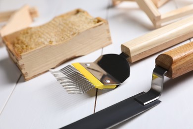 Photo of Honeycomb frame and beekeeping tools on white wooden table, closeup
