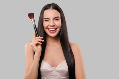 Happy woman with makeup brush on light grey background, space for text