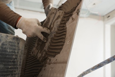 Photo of Worker applying cement on tile for installation in room, closeup