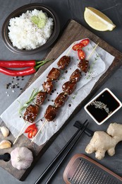 Photo of Skewers with pieces of tasty chicken meat glazed in soy sauce and other products on grey textured table, flat lay
