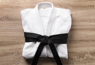 Martial arts uniform with black belt on wooden background, top view