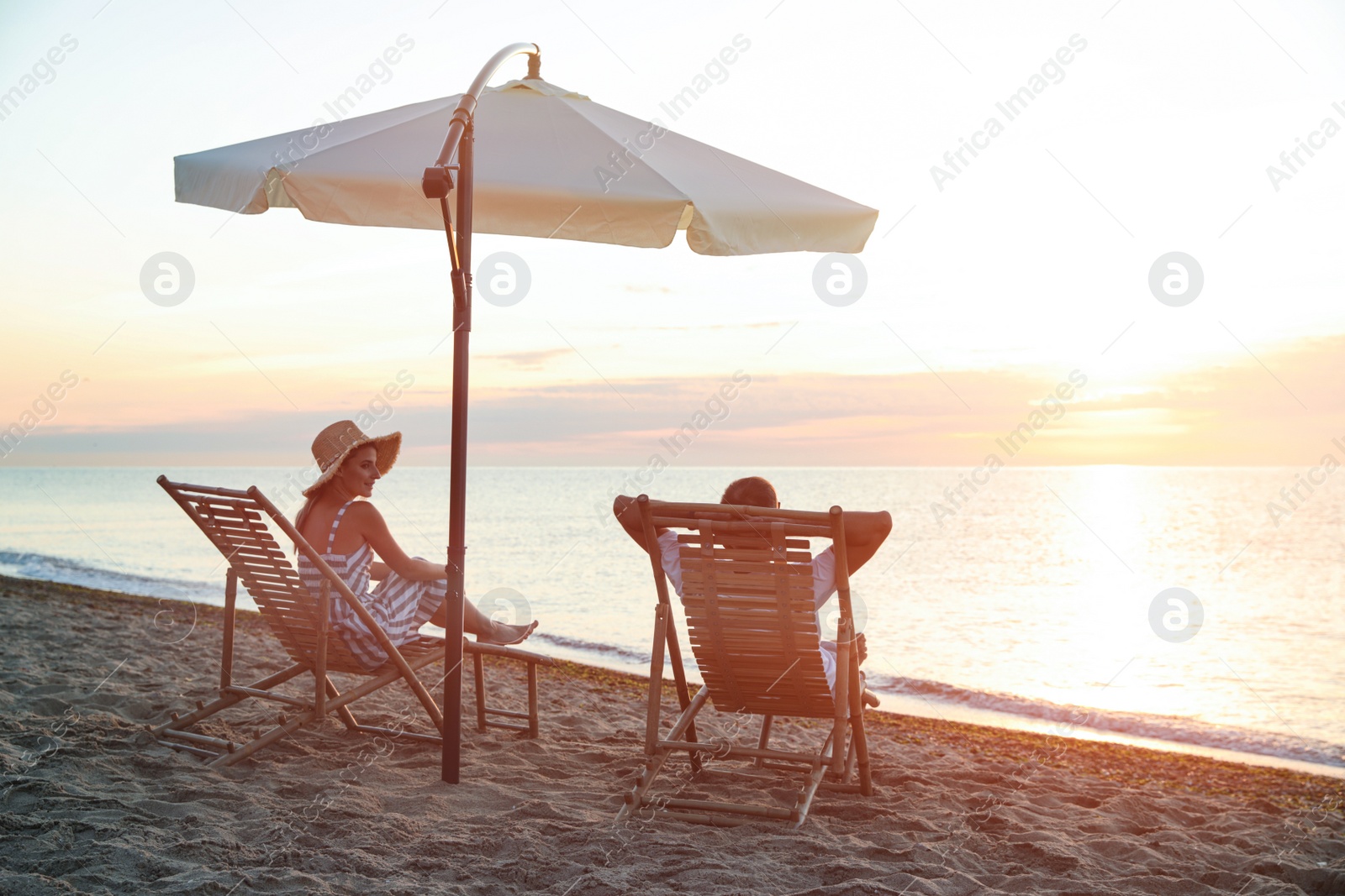 Photo of Couple relaxing on deck chairs at sandy beach. Summer vacation