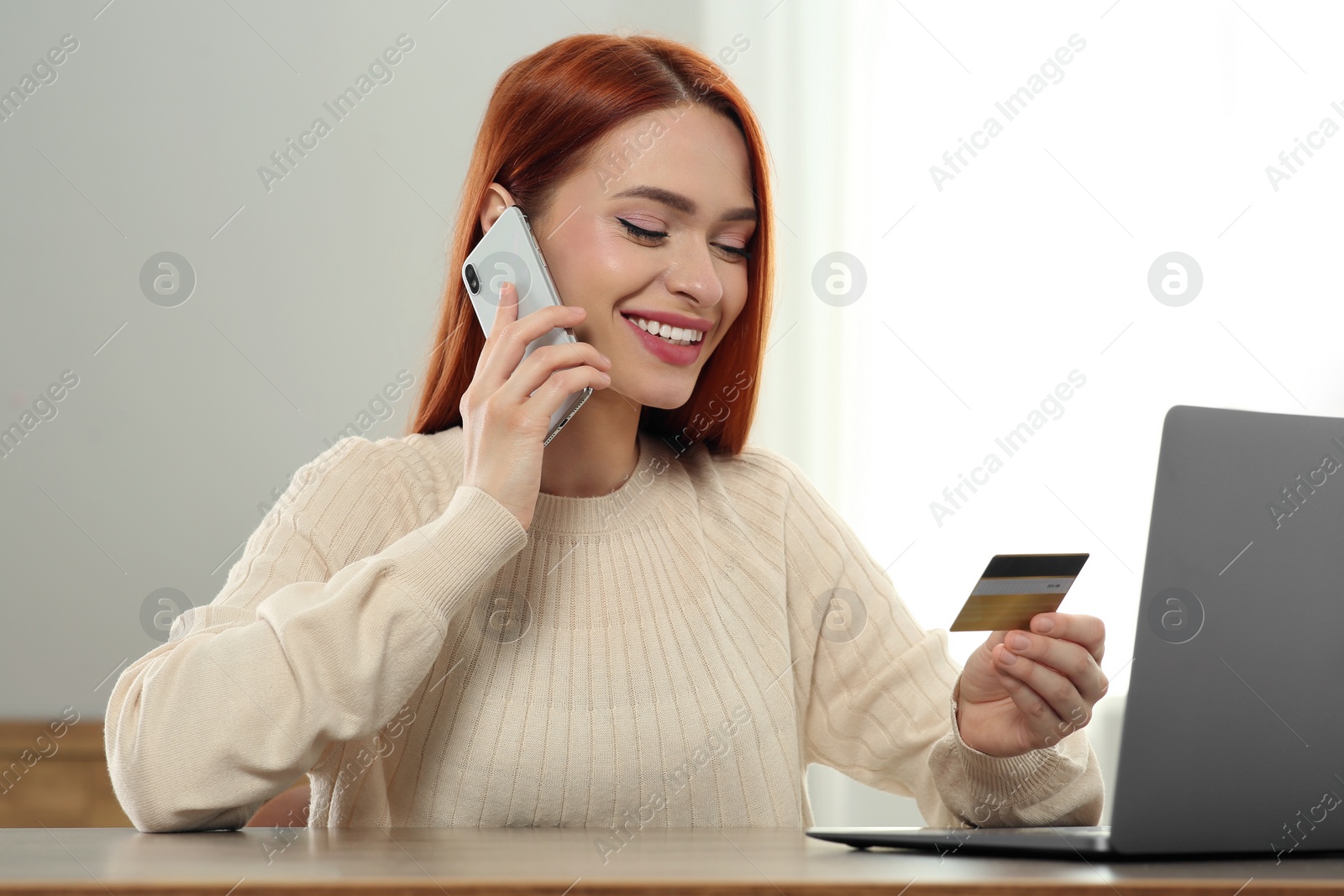 Photo of Happy woman with credit card using smartphone for online shopping at wooden table indoors