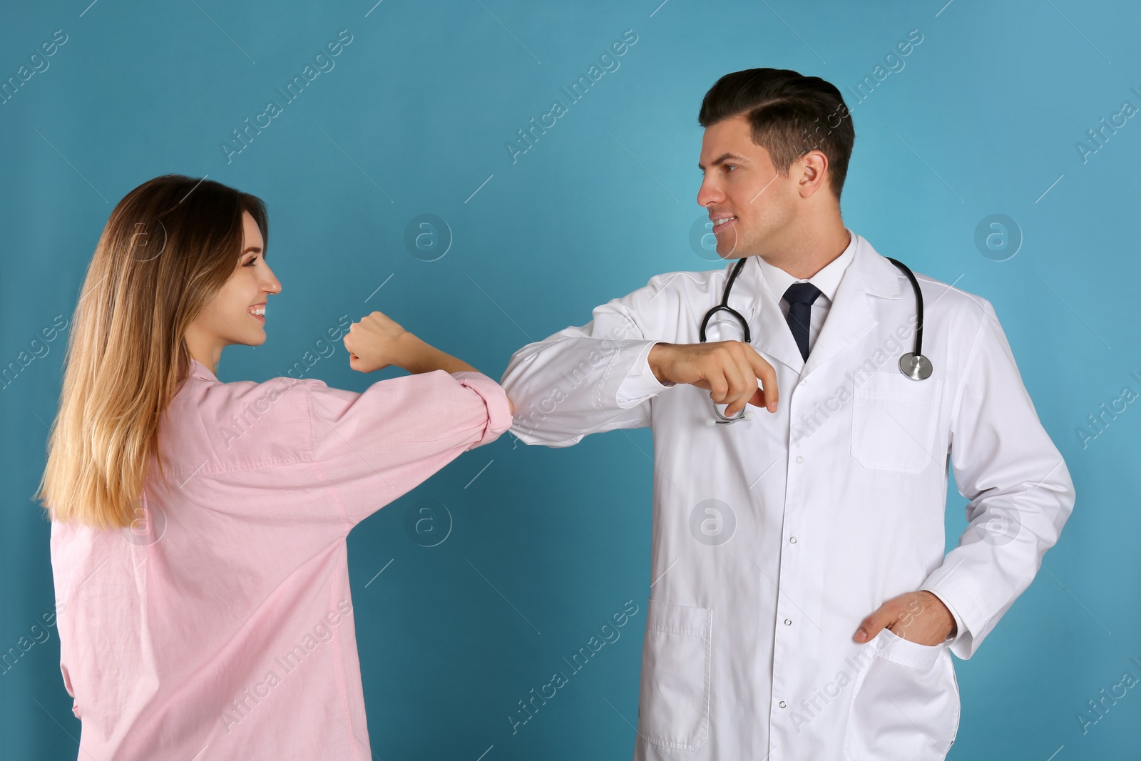 Photo of Doctor and patient doing elbow bump instead of handshake on light blue background. New greeting during COVID-19 pandemic