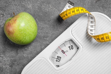 Photo of Scales, measuring tape and apple on gray background, closeup. Weight loss