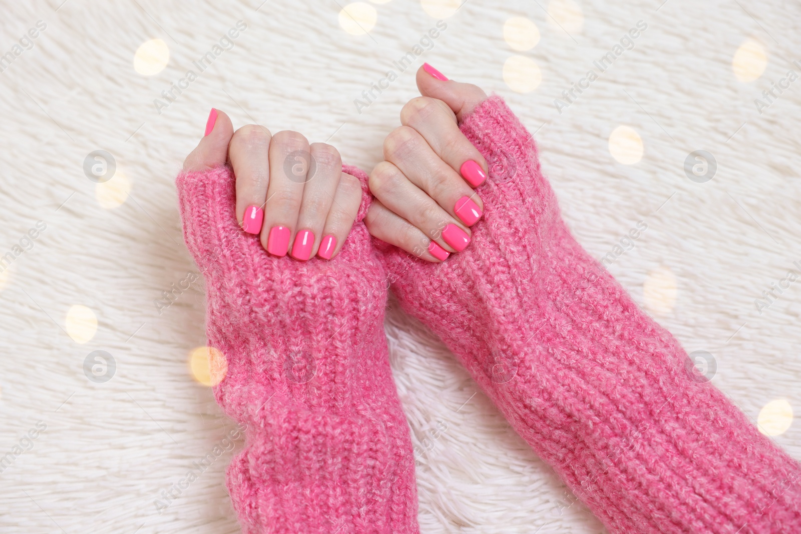 Photo of Woman showing her manicured hands with pink nail polish on faux fur mat, top view. Bokeh effect