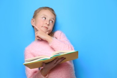 Photo of Little girl with book on light blue background. Space for text