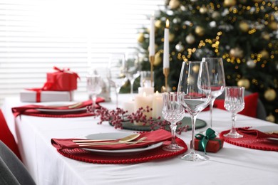 Christmas table setting with burning candles, gift box and dishware indoors