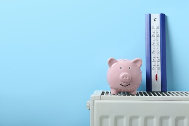 Piggy bank and thermometer on heating radiator near light blue wall. Space for text