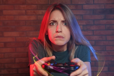 Photo of Emotional young woman playing video games with controller near brick wall