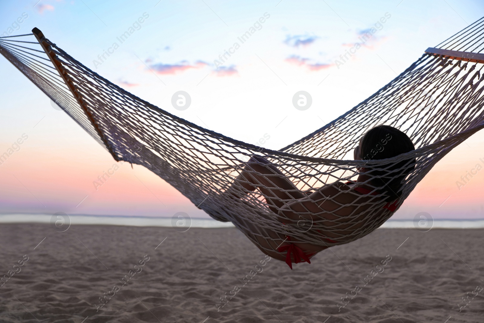 Photo of Young woman relaxing in hammock on beach at sunset