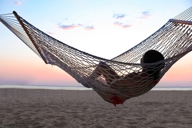 Young woman relaxing in hammock on beach at sunset