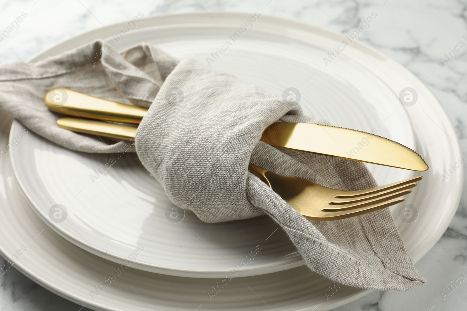 Photo of Stylish setting with cutlery, napkin and plates on white marble table, closeup