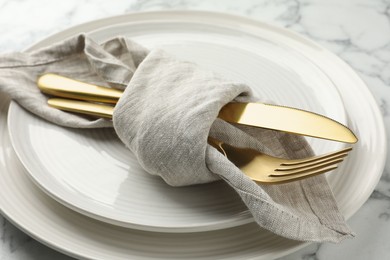 Stylish setting with cutlery, napkin and plates on white marble table, closeup