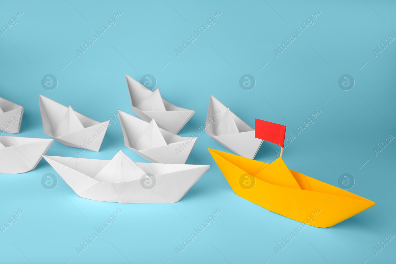 Photo of Group of paper boats following yellow one on light blue background. Leadership concept