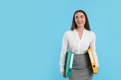Photo of Happy woman with folders on light blue background, space for text