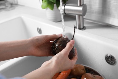 Photo of Woman washing fresh beetroot in kitchen sink, closeup. Cooking vinaigrette salad
