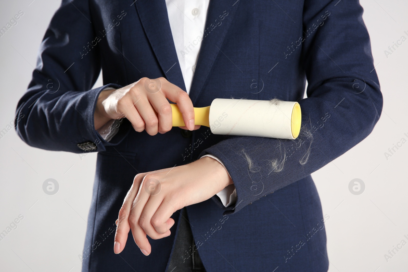 Photo of Woman removing cat hair from dark blue jacket with lint roller on grey background, closeup