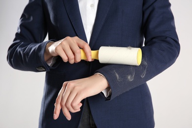 Woman removing cat hair from dark blue jacket with lint roller on grey background, closeup