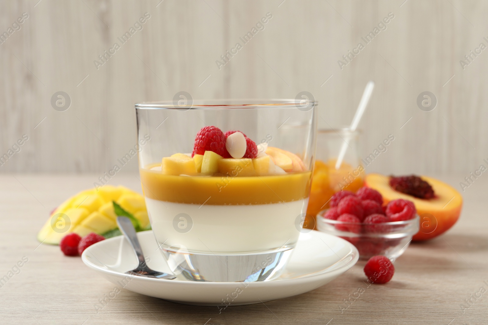 Photo of Delicious panna cotta with mango coulis, fresh fruit pieces and almond flakes on light wooden table